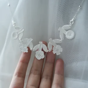 Handmade silver flower necklace draped over an open hand against sheer white fabric
