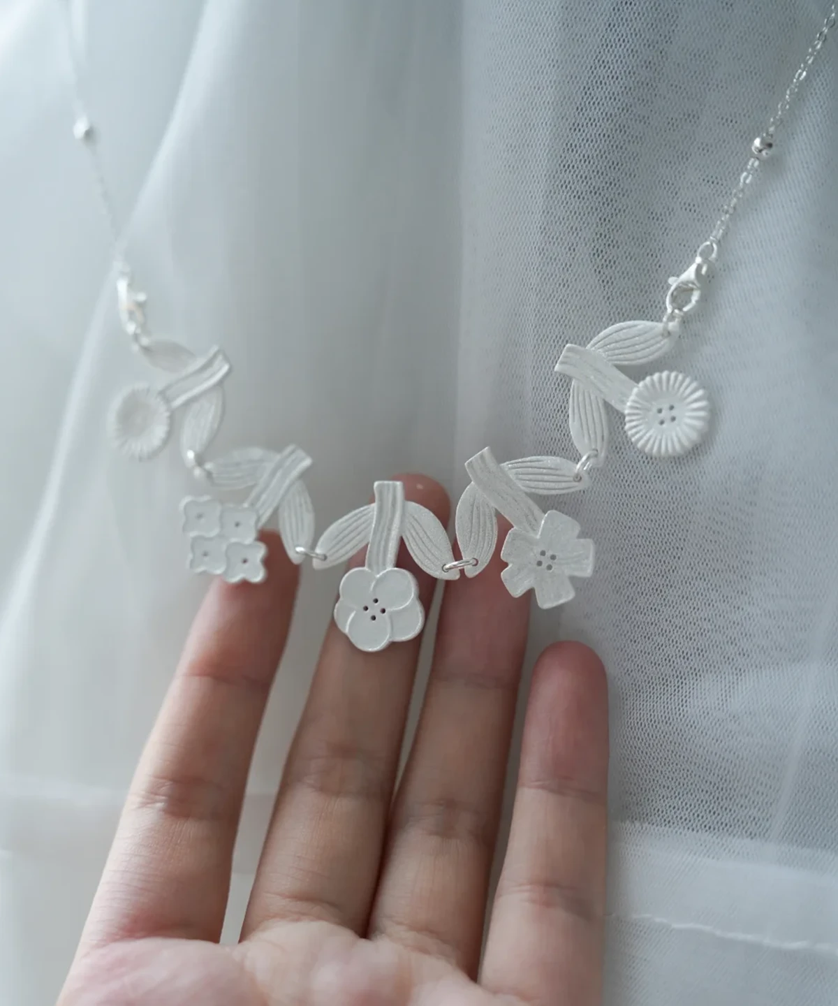 Handmade silver flower necklace draped over an open hand against sheer white fabric
