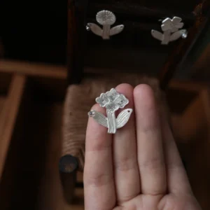 Handmade silver flower stud earring held in an open palm