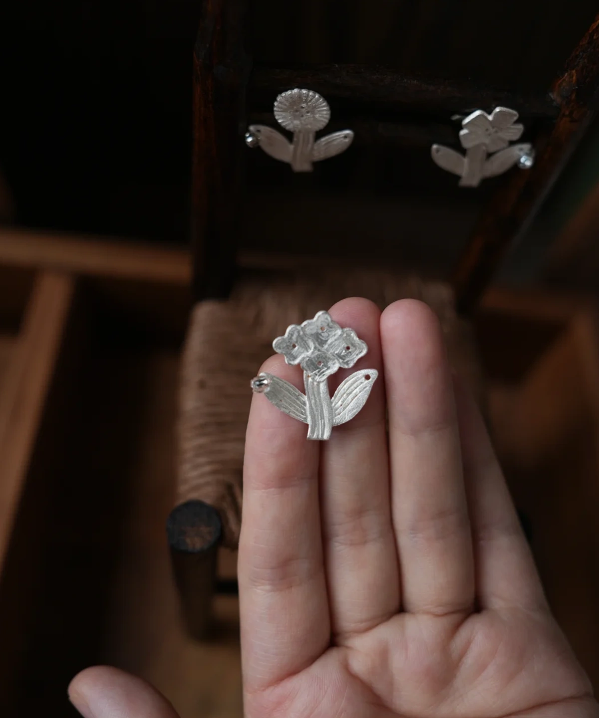 Handmade silver flower stud earring held in an open palm