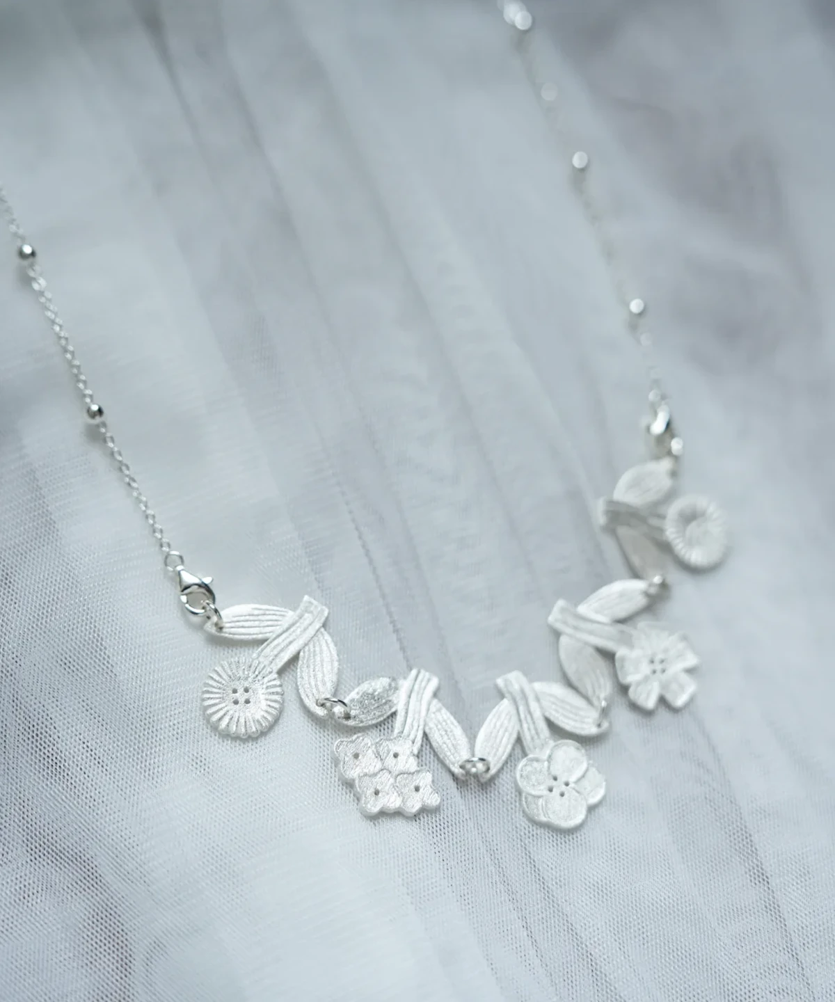 Morning Dew flower necklace in silver on sheer white fabric, garland of five flowers between leaf pairs