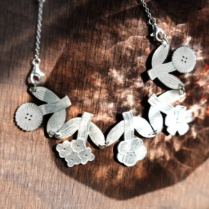 Silver flower necklace in dappled sunlight on dark wood — satin blooms, ribbed leaves, beaded chain