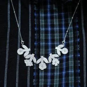 Silver flower necklace with linked blooms and leaves on dark plaid fabric, beaded chain
