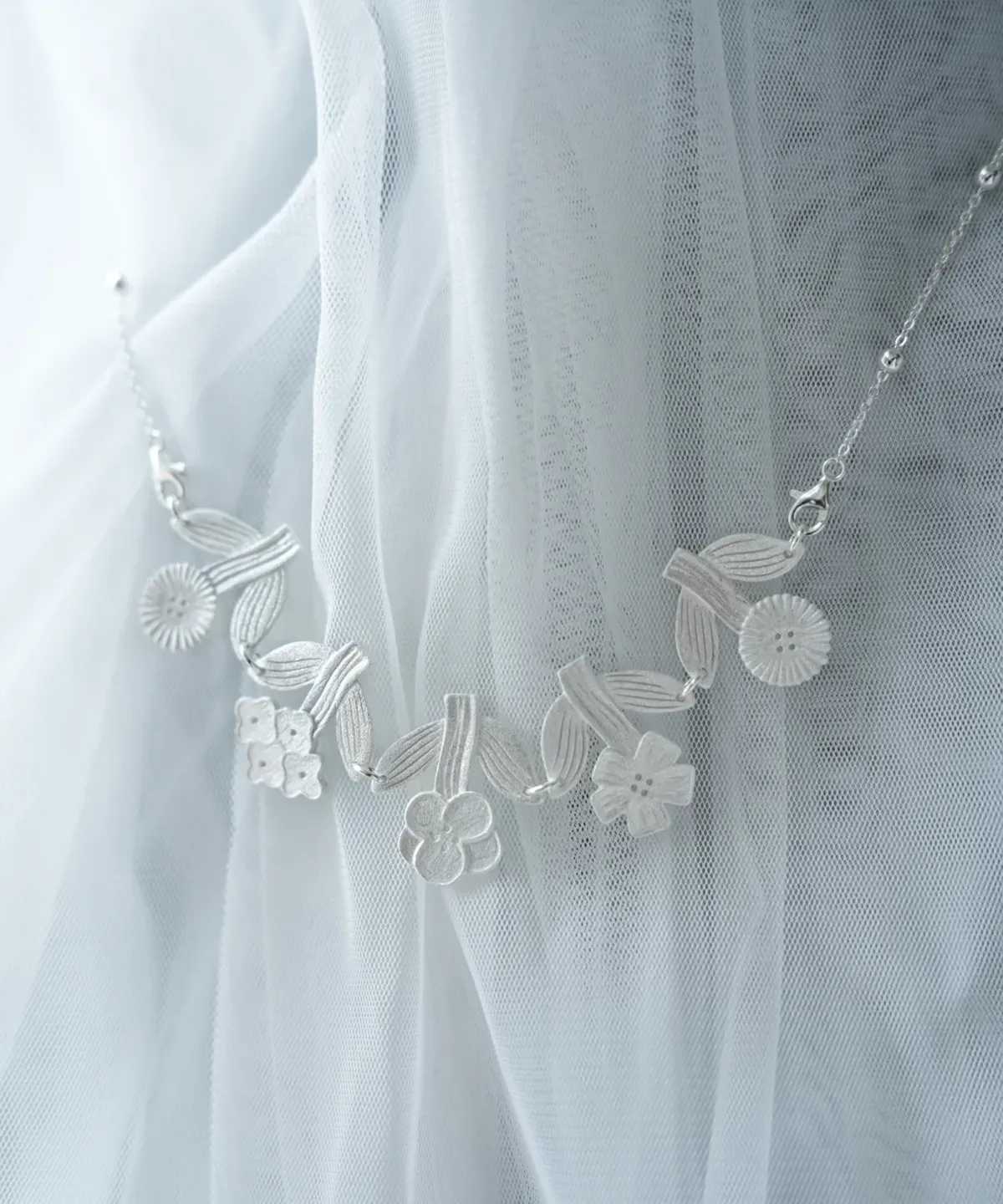 Silver flower necklace resting on white tulle, brushed blooms with a fine beaded chain