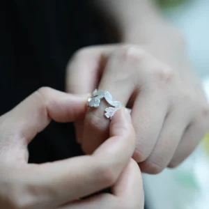 Hands holding a silver flower ring, open garland band between the fingers