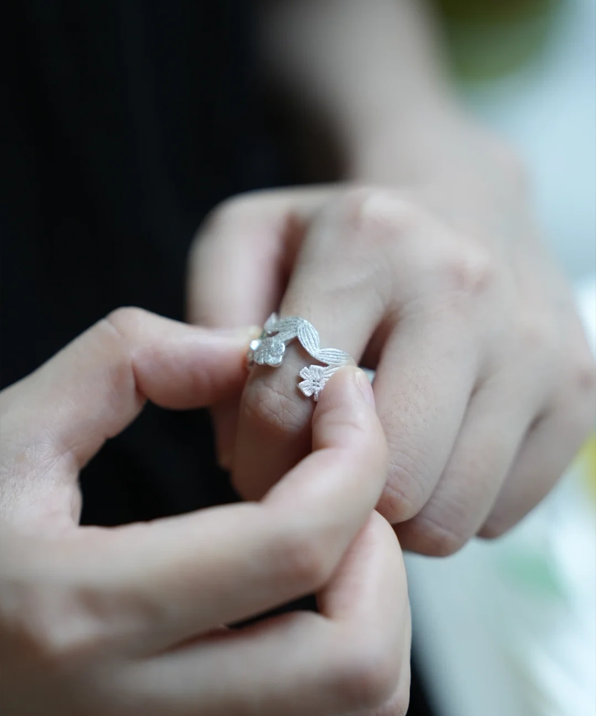 Hands holding a silver flower ring, open garland band between the fingers