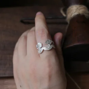 Silver flower ring worn on a hand resting over dark wood