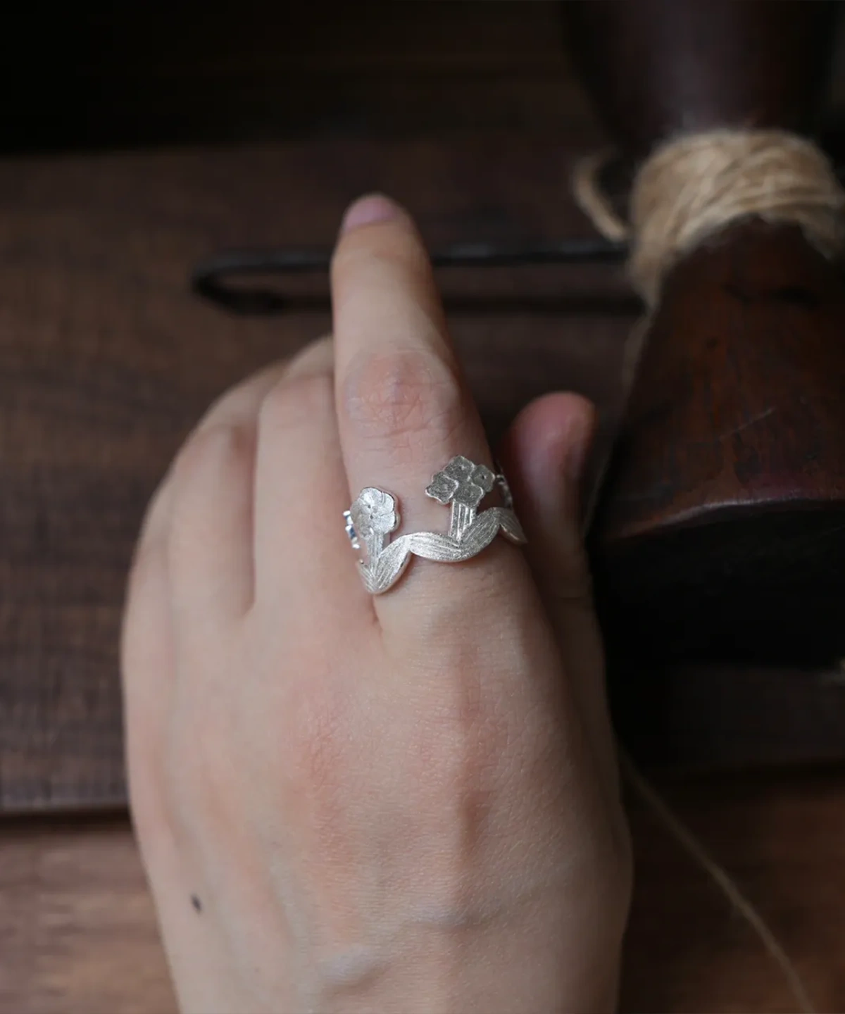 Silver flower ring worn on a hand resting over dark wood