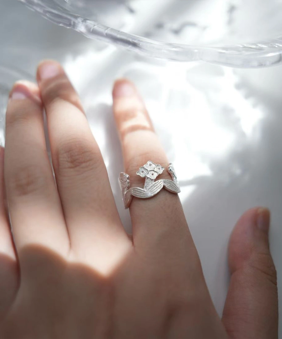 Silver flower ring worn on the finger in dappled sunlight, blooms and leaves circling the band