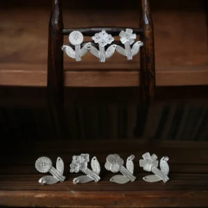 Four silver flower stud earrings arranged on a miniature wooden stand