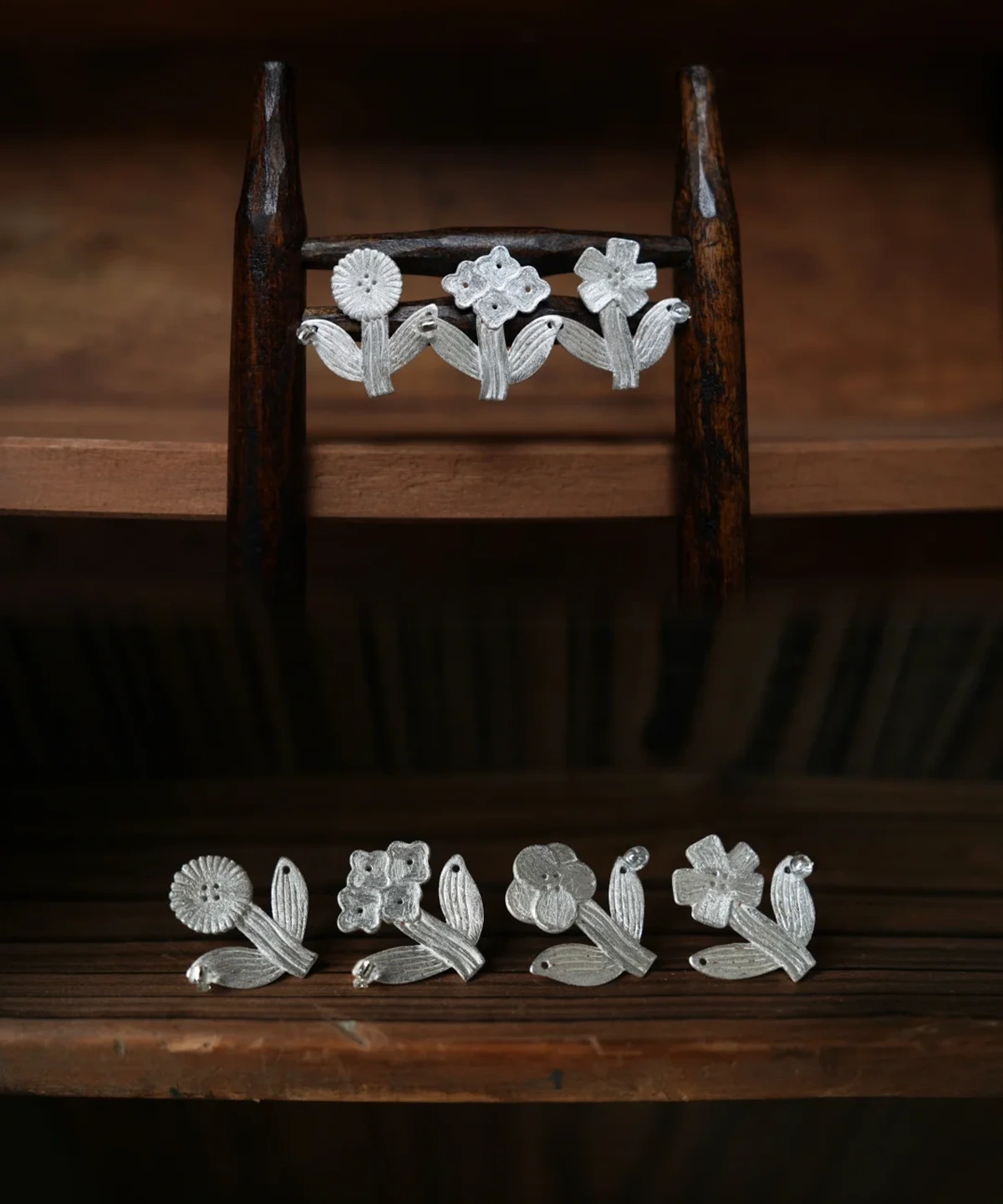 Four silver flower stud earrings arranged on a miniature wooden stand