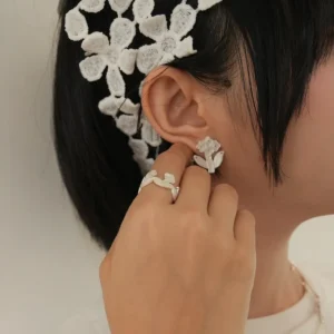 Model wearing small silver flower stud earrings, hand raised beside the ear