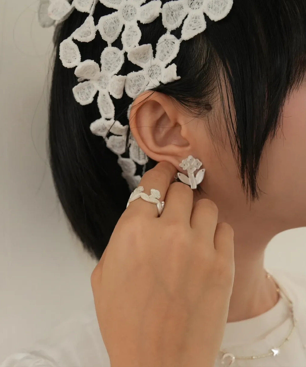 Model wearing small silver flower stud earrings, hand raised beside the ear