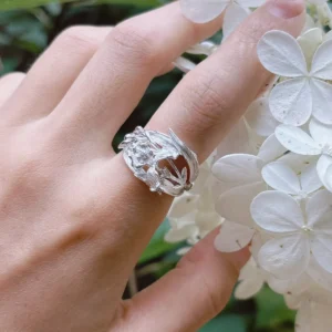 Silver iris ring in polished S925, worn on the hand beside white blossoms, cast blooms and blade leaves