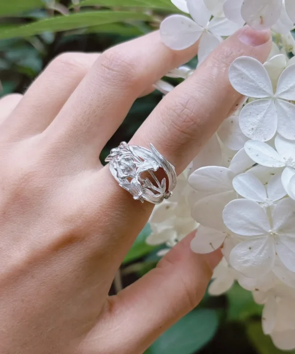 Silver iris ring in polished S925, worn on the hand beside white blossoms, cast blooms and blade leaves