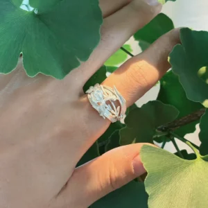 Handmade iris flower ring in S925 sterling silver worn in sunlight against ginkgo leaves