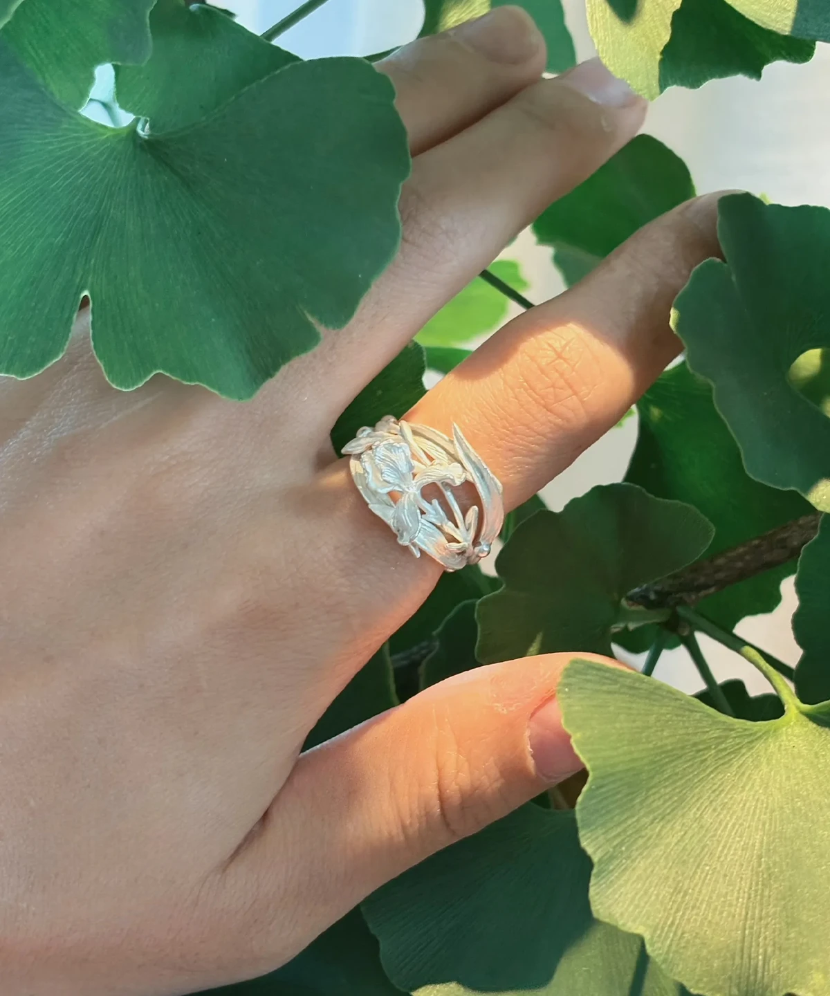 Handmade iris flower ring in S925 sterling silver worn in sunlight against ginkgo leaves
