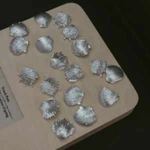 Silver shell earrings in 990 pure silver, hand-cast shells laid out across a wooden bench board
