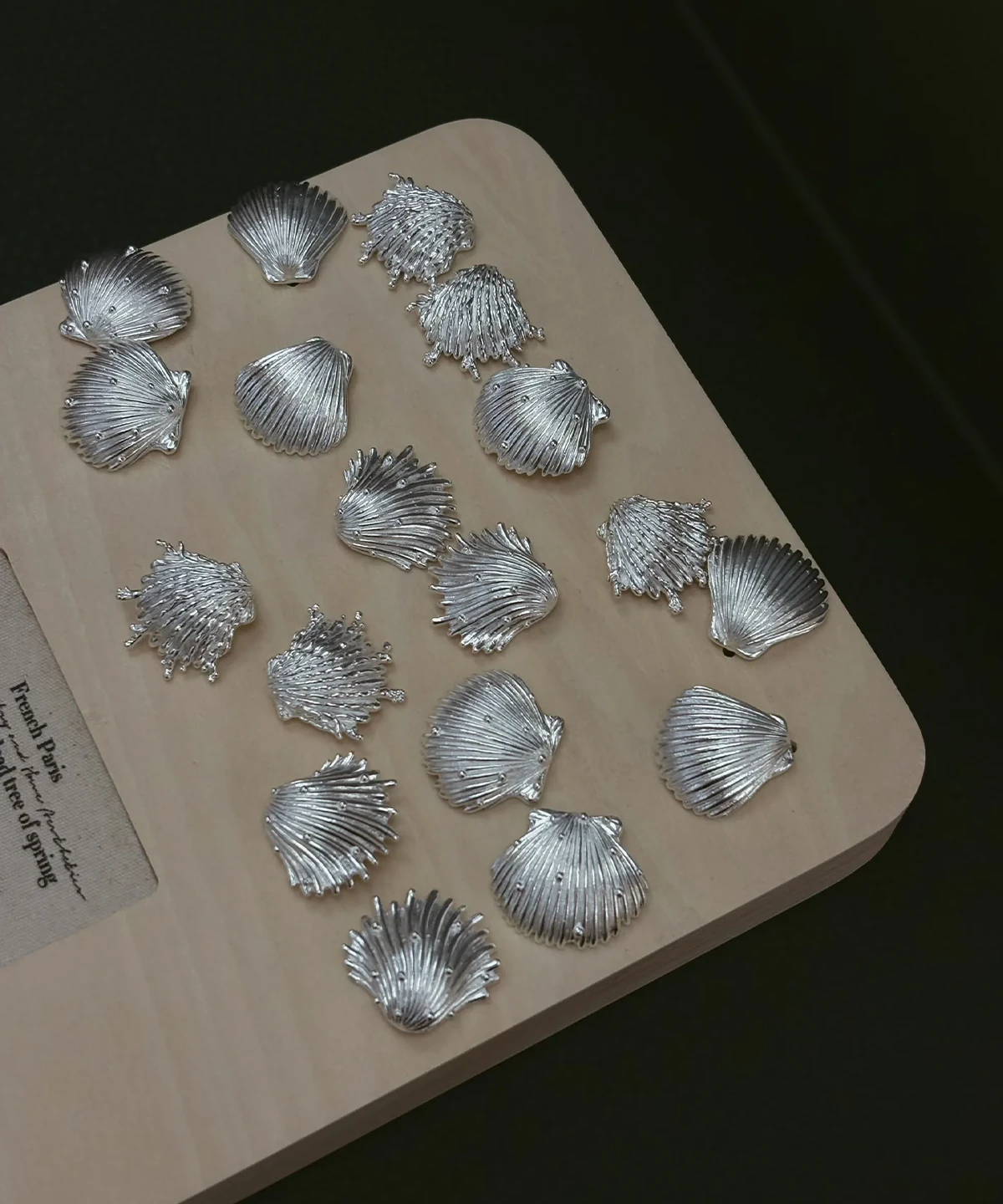 Silver shell earrings in 990 pure silver, hand-cast shells laid out across a wooden bench board