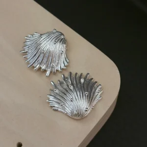 Fringed fan and whirled silver shell earrings in 990 pure silver on a pale wood board