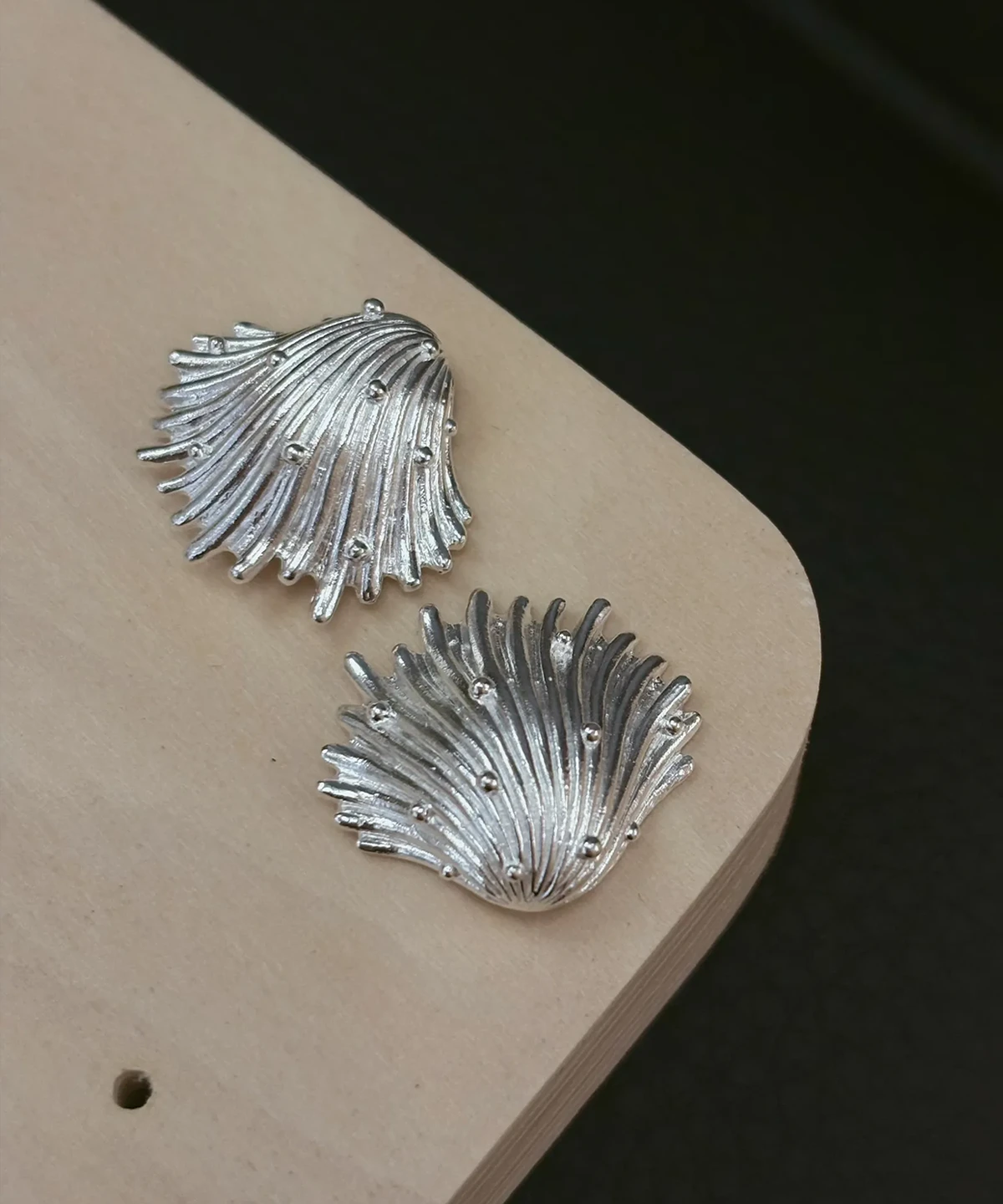 Fringed fan and whirled silver shell earrings in 990 pure silver on a pale wood board