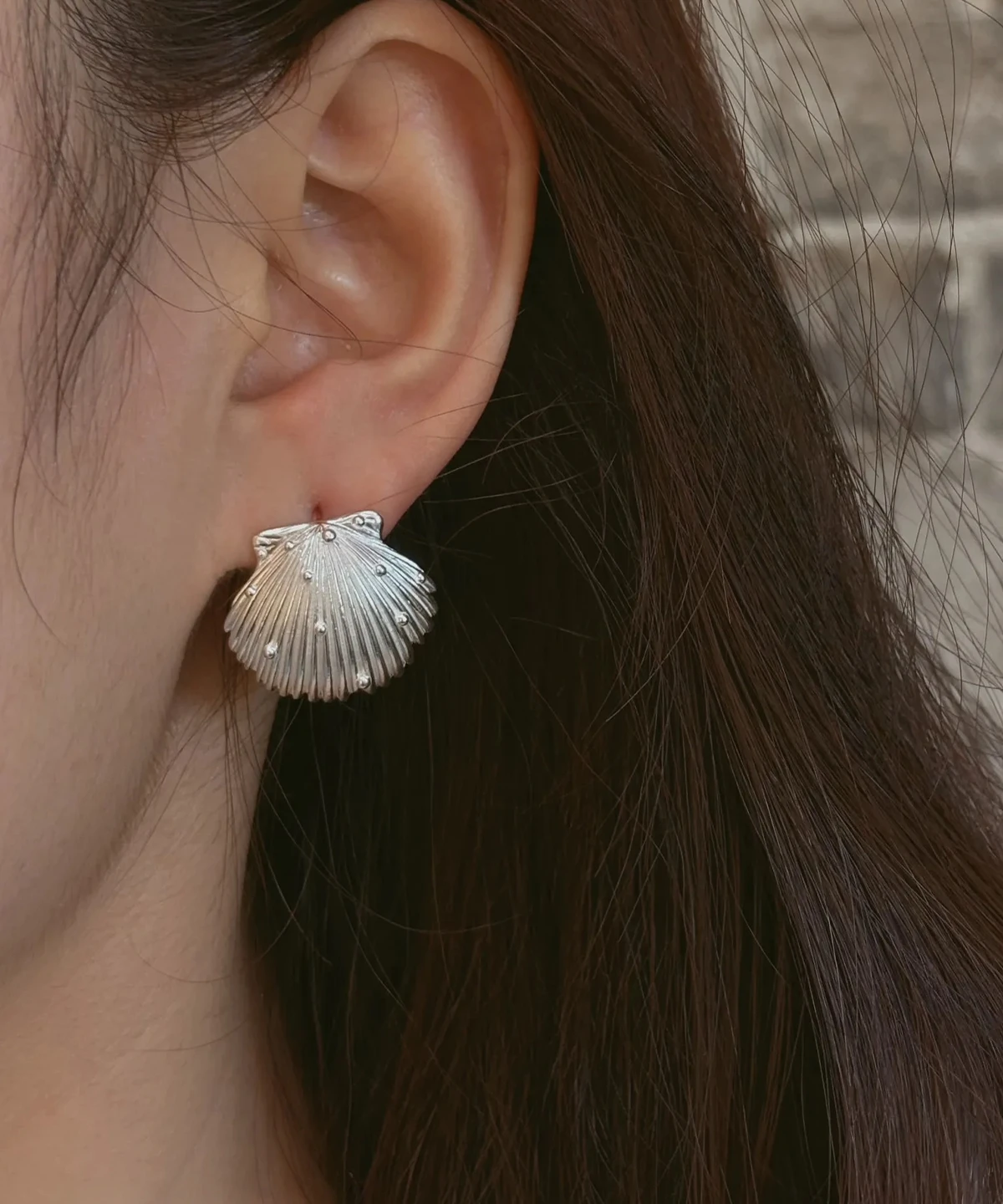 Ribbed scallop silver shell earrings worn on the ear, a 990 pure silver stud filling the lobe