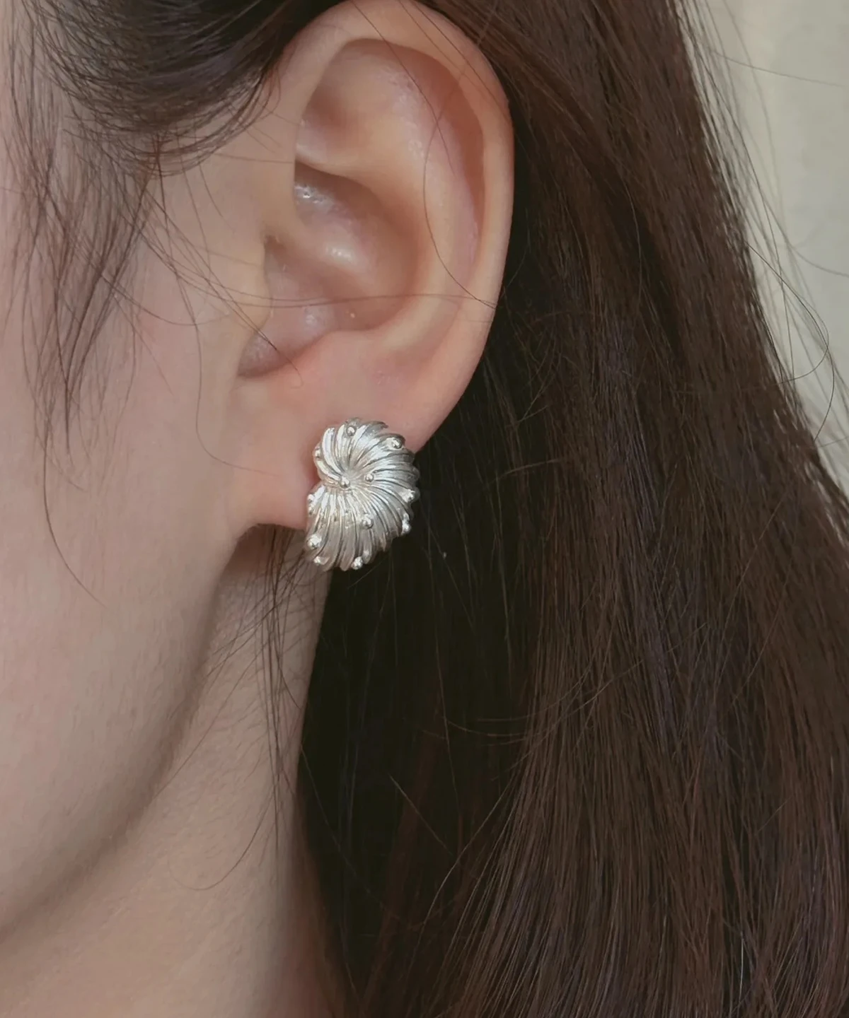 Whirled shell stud earrings worn on the ear, silver ribs turning around a single point