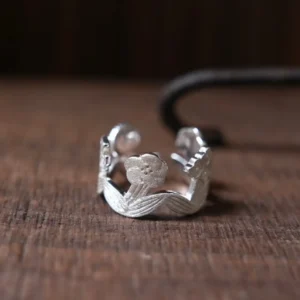Sterling silver flower ring on dark wood — small blooms and ribbed leaves joined into an open garland