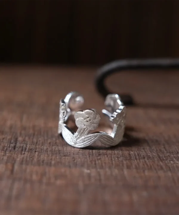 New In 2 Sterling silver flower ring on dark wood — small blooms and ribbed leaves joined into an open garland