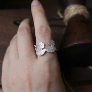 Sterling silver flower ring worn on the finger, dark wooden tools behind