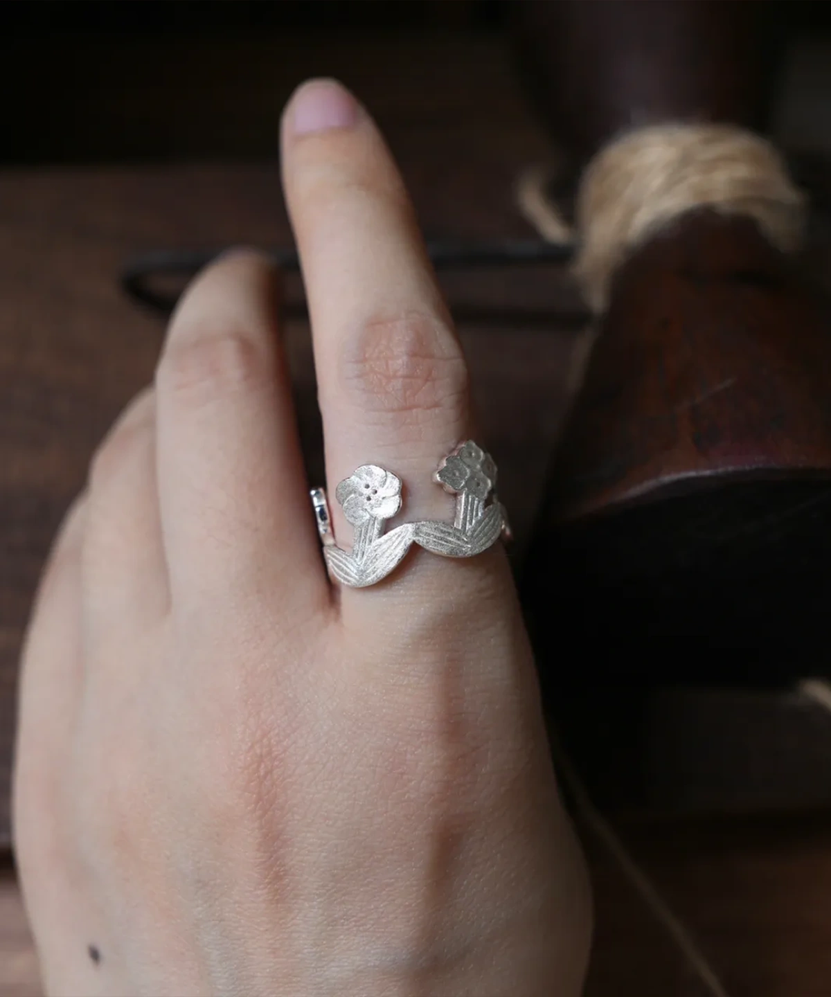 Sterling silver flower ring worn on the finger, dark wooden tools behind