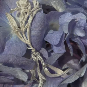Silver iris floral dangle earring photographed among purple petals with carved flower and leaf detail