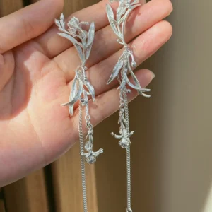 Long iris floral dangle earrings in sterling silver held in one hand to show scale and asymmetric design