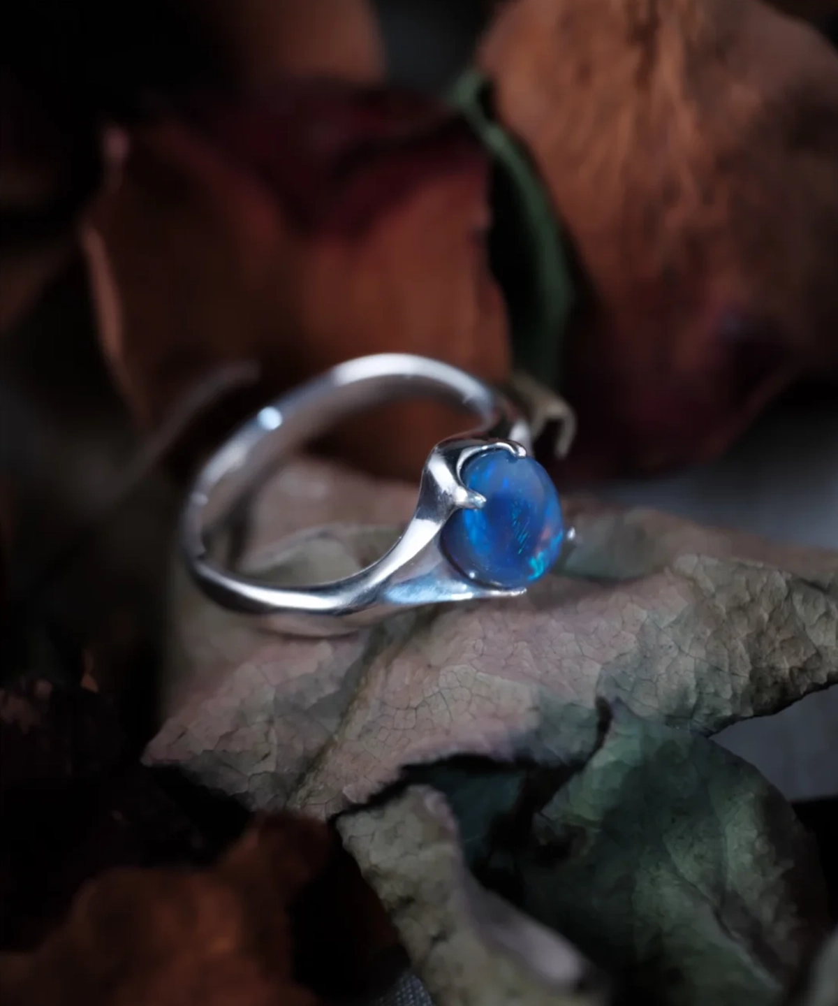 Natural blue opal ring in handcrafted S925 sterling silver displayed on dried leaves