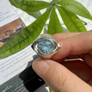 Hand holding a Six Eyes Ring with a faceted blue topaz stone and sculptural S925 silver setting