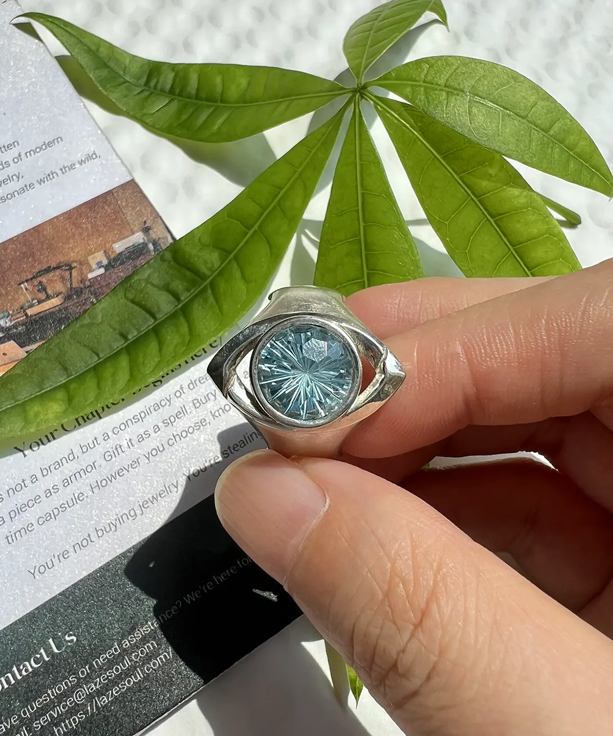 Hand holding a Six Eyes Ring with a faceted blue topaz stone and sculptural S925 silver setting