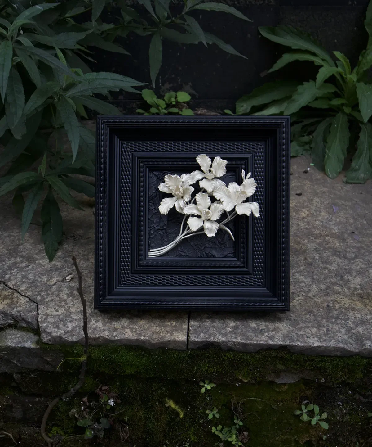 Framed silver iris floral artwork photographed among deep green garden foliage