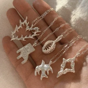 Close view of five handmade 999 silver pendant necklaces arranged across a hand in sunlight