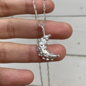 Textured crescent moon pendant in 999 fine silver on a rectangular-link silver chain held over a hand