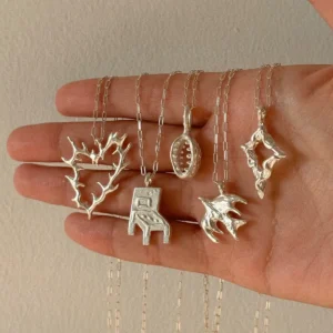 Five handmade 999 silver pendant necklaces in heart, chair, oval, bird and star forms displayed on a hand