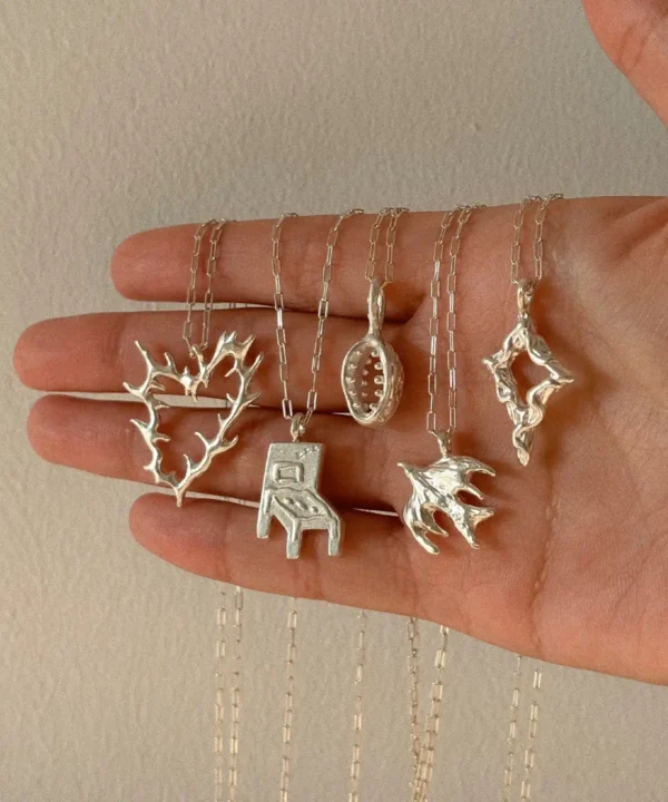 Five handmade 999 silver pendant necklaces in heart, chair, oval, bird and star forms displayed on a hand