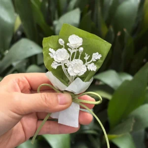 Hand holding the three-bloom 950 silver poppy bouquet in green and white paper