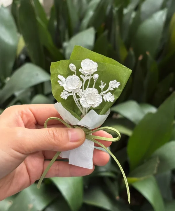 Hand holding the three-bloom 950 silver poppy bouquet in green and white paper