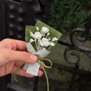 Hand holding a three-bloom silver poppy bouquet beside a dark iron garden bench