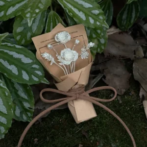 Two-bloom 950 silver poppy bouquet in kraft paper resting among moss and patterned leaves