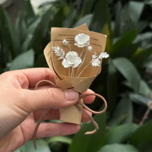Hand holding the two-bloom 950 silver poppy bouquet in kraft paper against green foliage