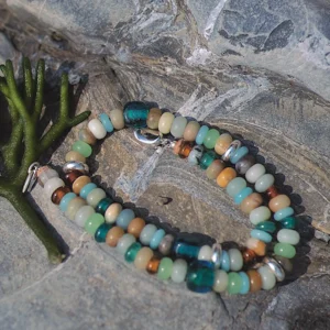Amazonite necklace coiled on a textured rock beside green seaweed