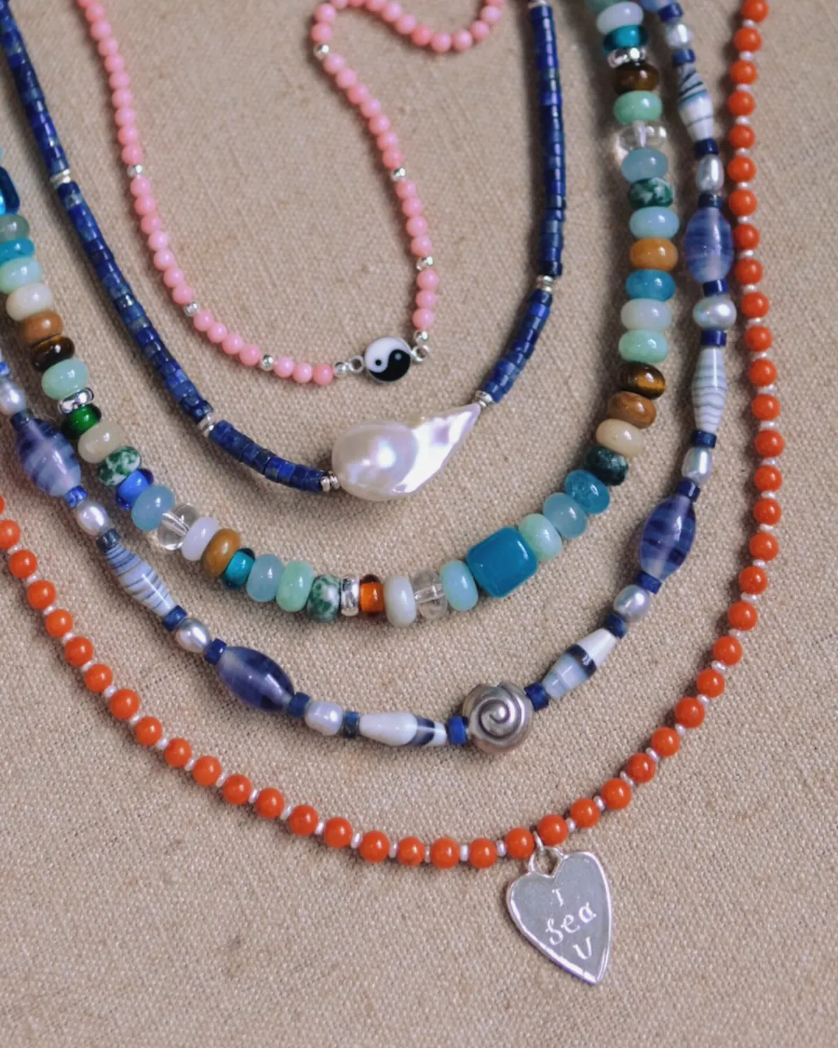 Necklace Layering Colour and Structure Flat Lay Colourful bead and silver necklaces arranged in graduated curves on linen