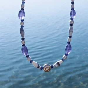 Blue agate necklace with a silver spiral shell centre held above clear sea water