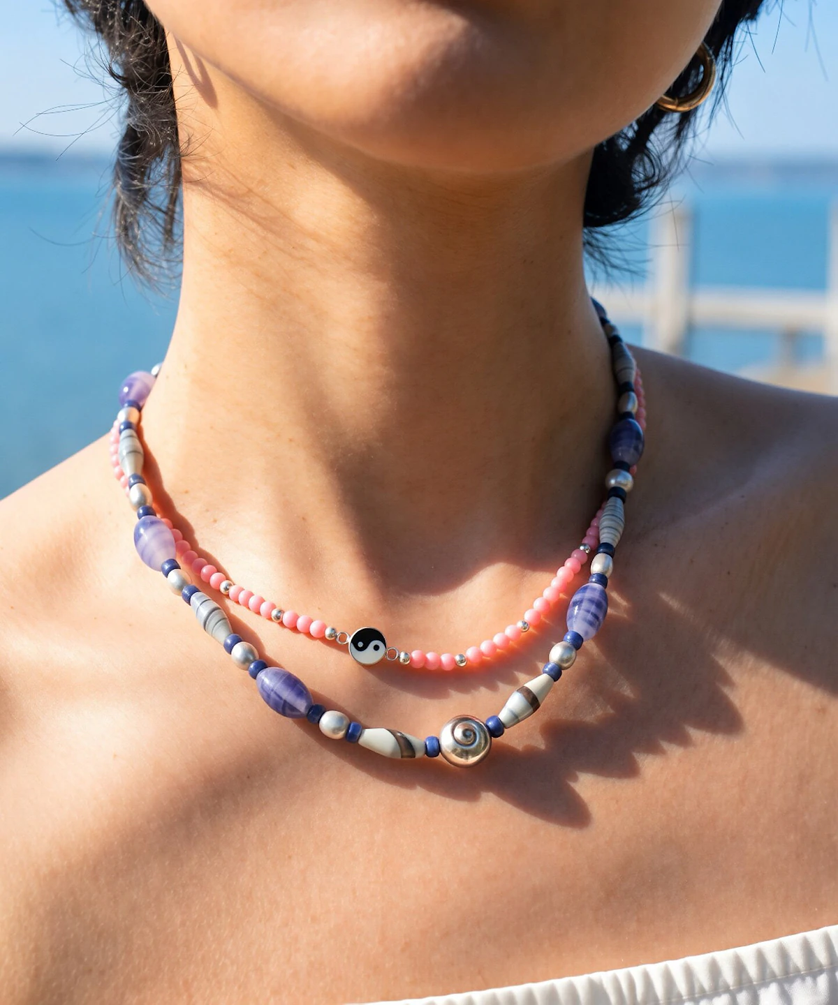 Blue agate and silver spiral shell necklace layered with pink beads in sunlight